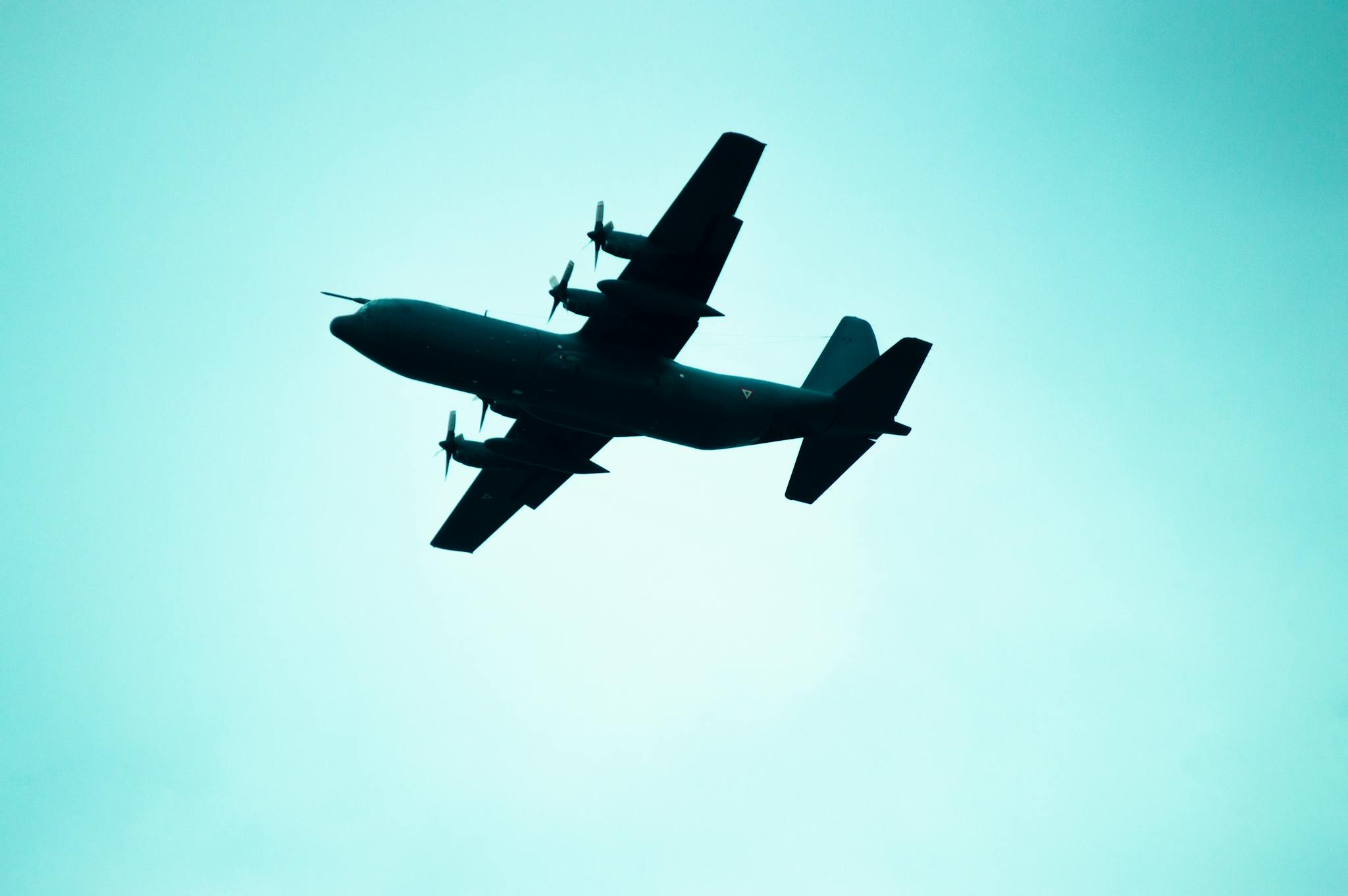 A silhouette of a military plane flying in a clear, blue sky, highlighting its aerodynamic design.
