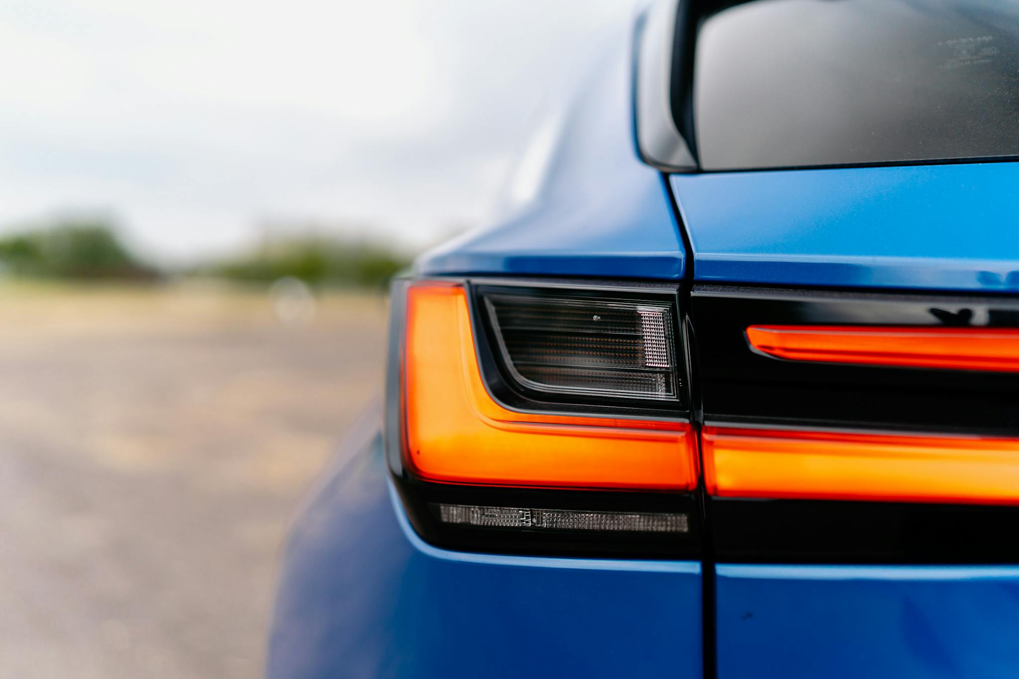 Detailed view of a vibrant blue car's taillight with a modern design, illuminated at dusk.